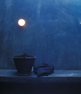 A Flos Glo-Ball Zero wall sconce mounted to concrete wall illuminating a pail and coat on a bench below.