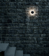 A single outdoor Flos Bellhop wall light mounted to a brick wall, illuminating a staircase below.