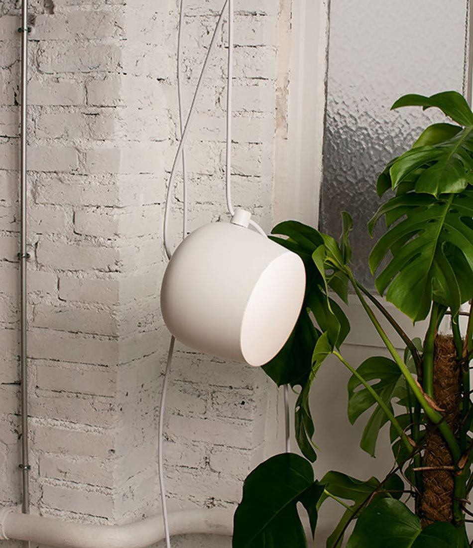 White Flos AIM suspension lamp hangs next to a tropical plant beside a brick wall.