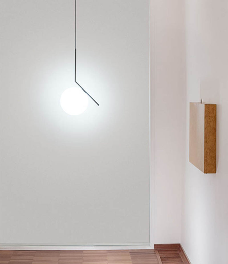 Flos IC Lights suspension lamp hanging in front of a glass panel in a room with wood floors.