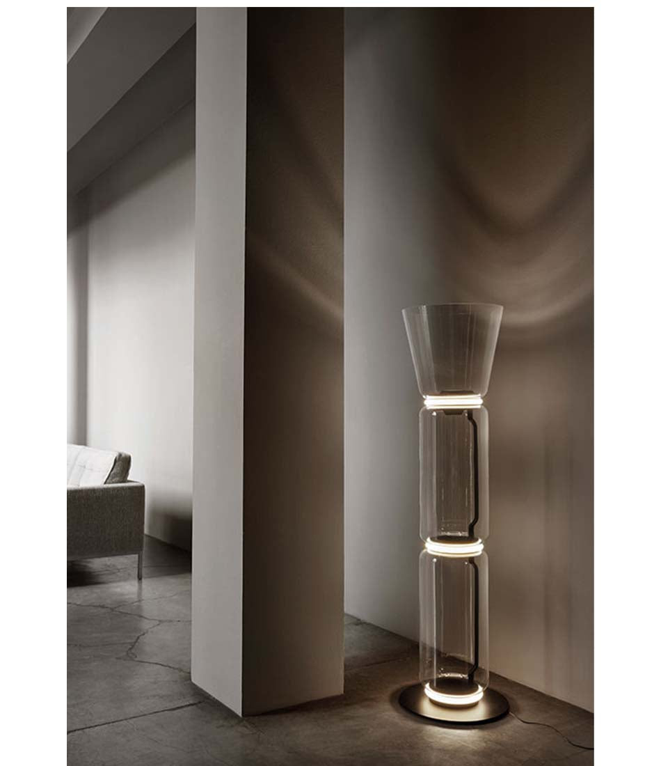 Flos Noctambule floor lamp. Glass cone top on 2 glass cylinder body next to a pillar.