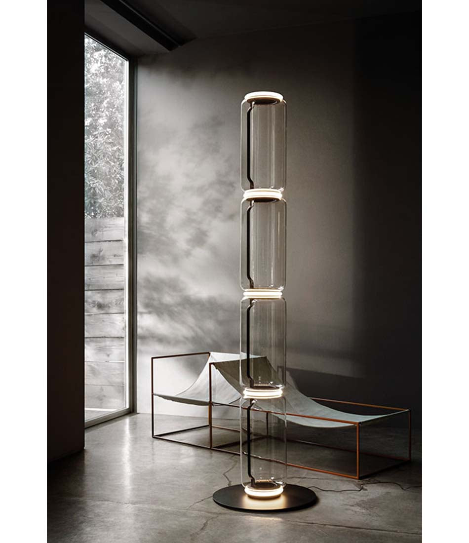 Flos Noctambule floor lamp with four glass cylinder body in front of an art sculpture.