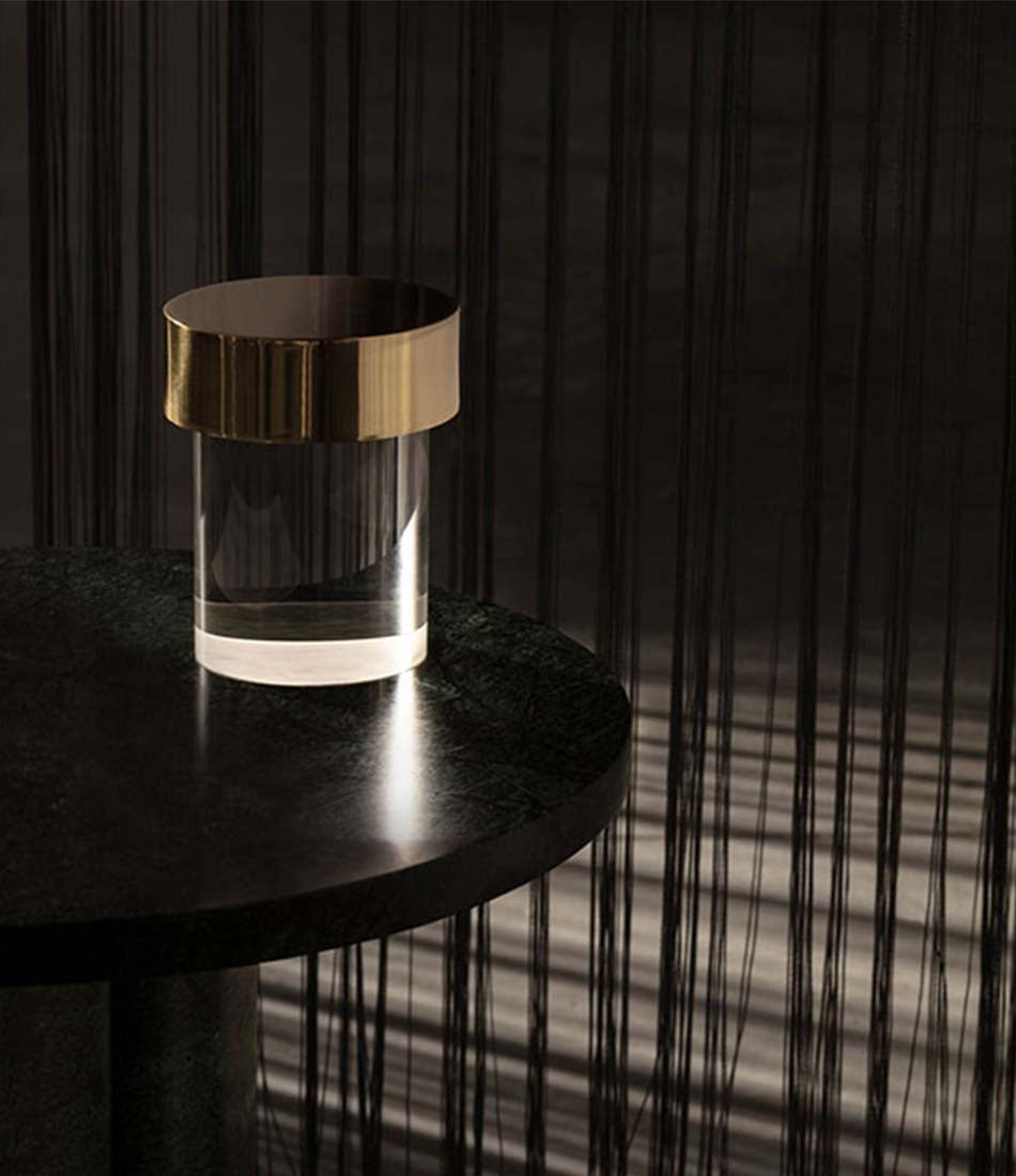 Polished Brass Flos Last Order table lamp on a round table in a dark room.