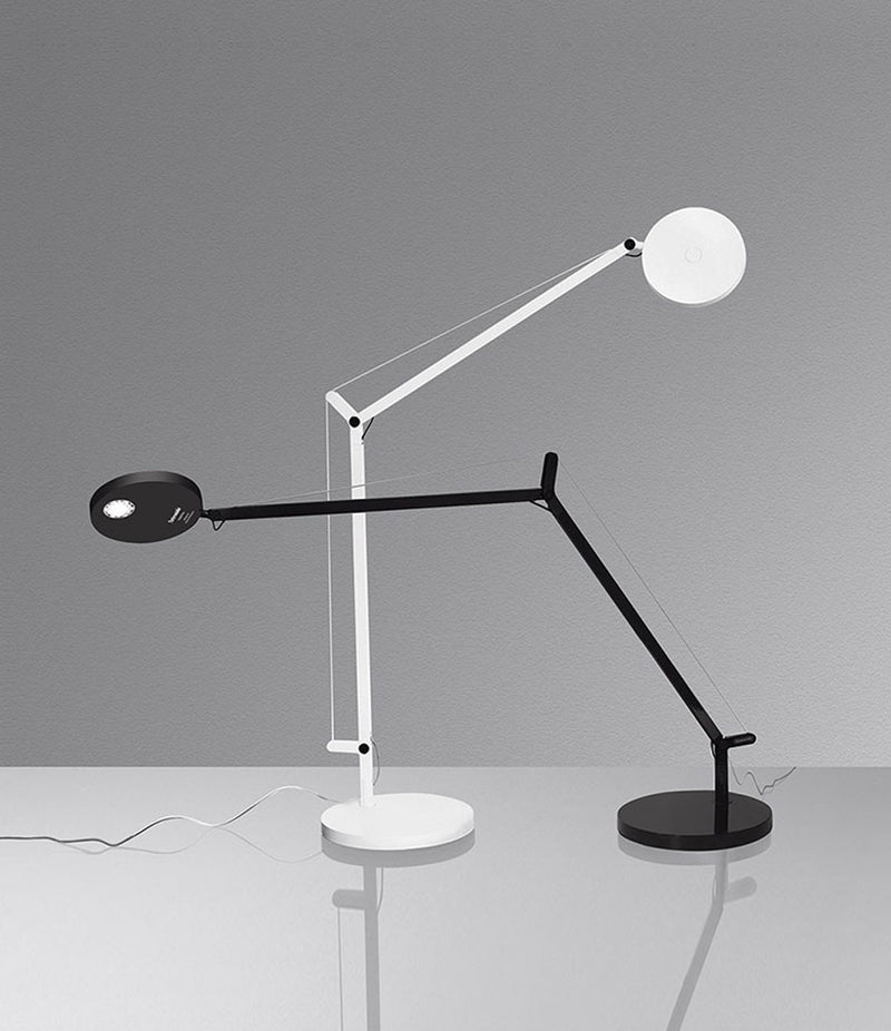 A white and a black Artemide Demetra table lamp side by side on a table.