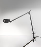 An Anthracite Grey Artemide Demetra table lamp with clamp, mounted to a desk.
