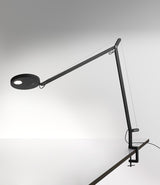 A black Artemide Demetra table lamp with clamp, mounted to a desk.
