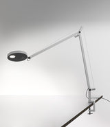 A white Artemide Demetra table lamp with clamp, mounted to a desk.
