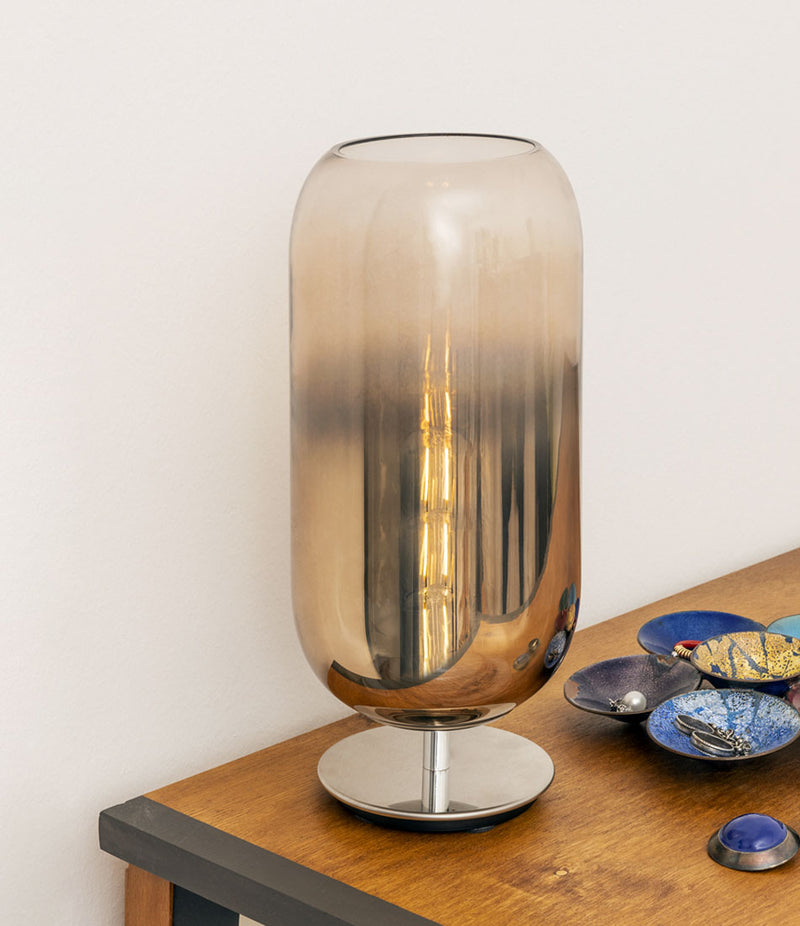 Pill-shaped Artemide Gople table lamp on a wooden table beside small decorative plates.
