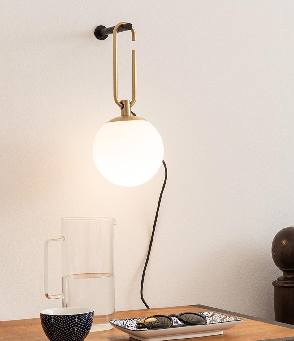Artemide NH Wall Lamp hangs above a table containing dishes and sunglasses.
