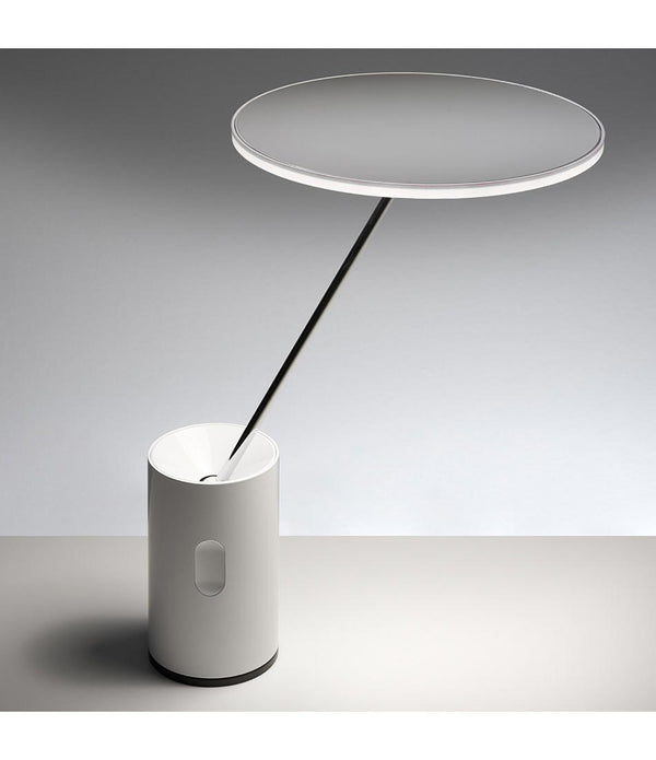 Artemide Sisifo table lamp, with disc-shaped lamp head atop stem in tilted position.