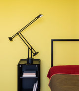 Double-hinged Artemide Tizio table lamp on a bedside table next to a bed.