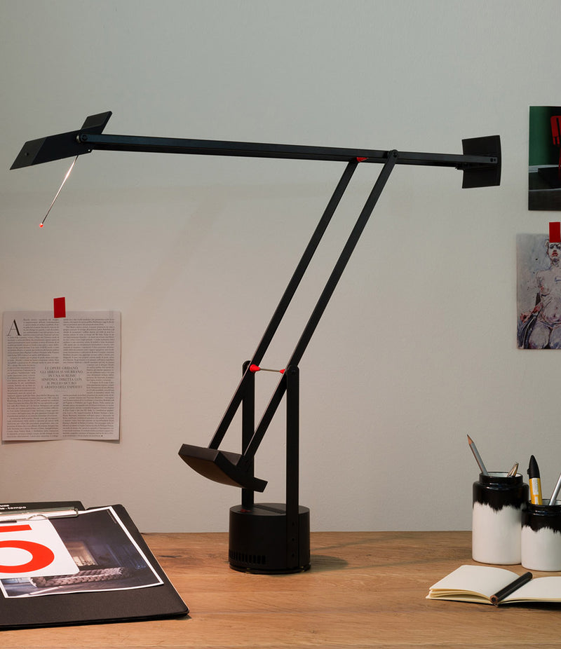 Artemide Tizio table lamp illuminates a magazine page on a wooden desk.