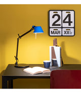 Artemide Tolomeo Bi-Color lamp with blue shade on a table above an open book.