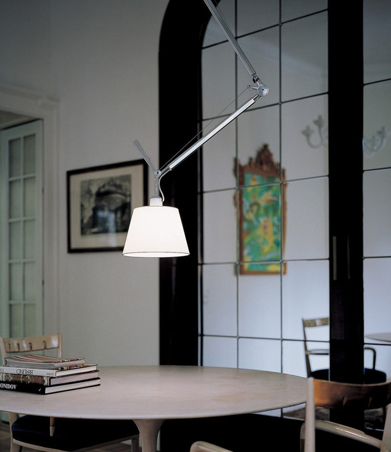 Artemide Tolomeo Off-Center with shade suspension lamp hangs above a stack of books on a dining table.