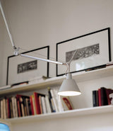 Artemide Tolomeo Off-Center suspension lamp angles down from the ceiling in front of a wall with books and picture frames.