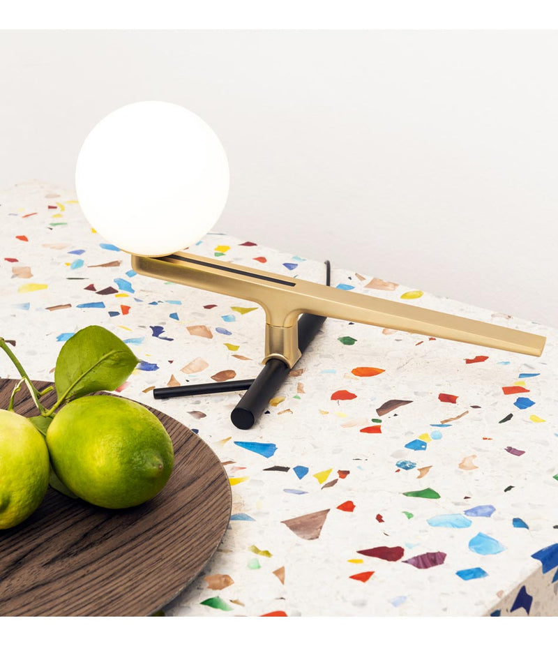 Artemide Yanzi table lamp on a multi-colored surface beside a bowl of limes.