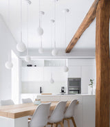 A grouping of Artemide Castore Suspension lamps hangs over a wood dining table in a modern kitchen.