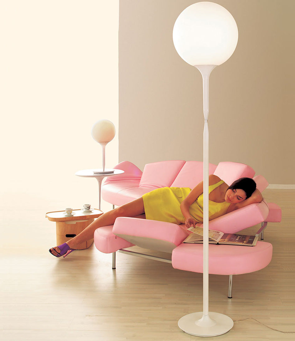 Artemide table lamp and floor lamp beside a woman reading a magazine on a sofa.