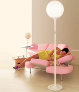 Artemide table lamp and floor lamp beside a woman reading a magazine on a sofa.