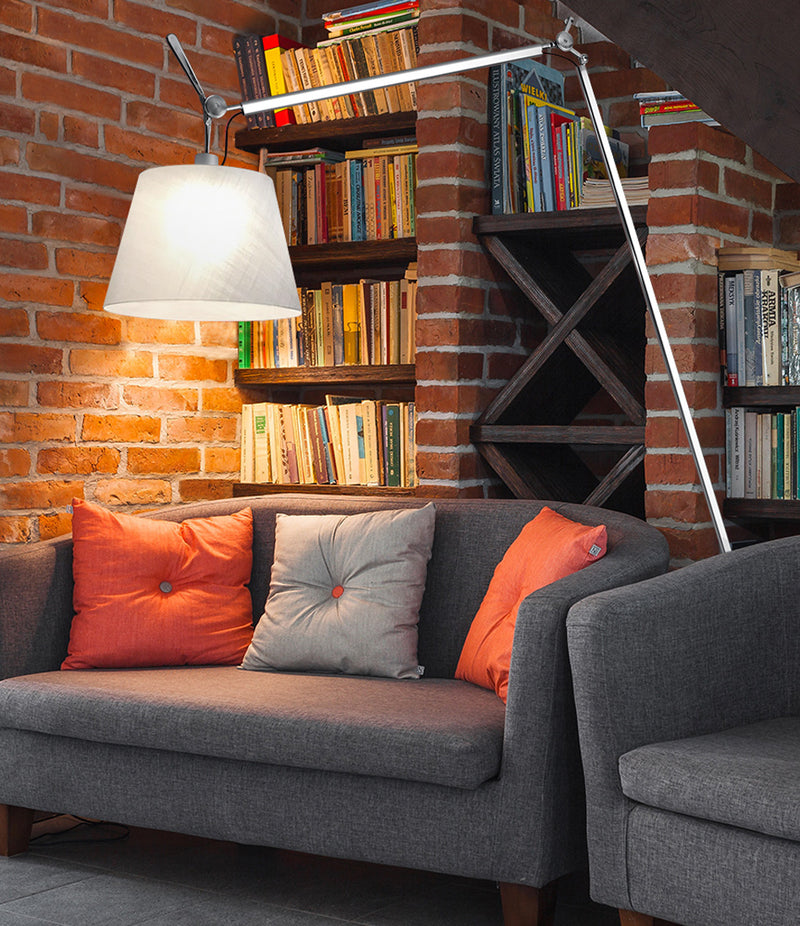 Artemide Tolomeo Maxi floor lamp over a sofa, in front of a bookshelf and brick wall.