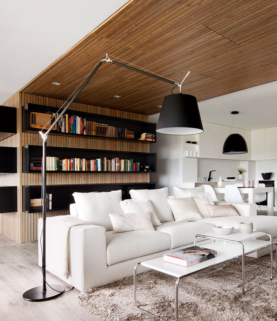 Black Artemide Tolomeo Mega floor lamp in a living room with sectional and wooden wall.