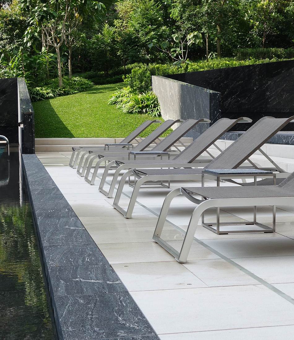 A row of Coro L3 sun loungers in charcoal grey fabric next to a swimming pool.