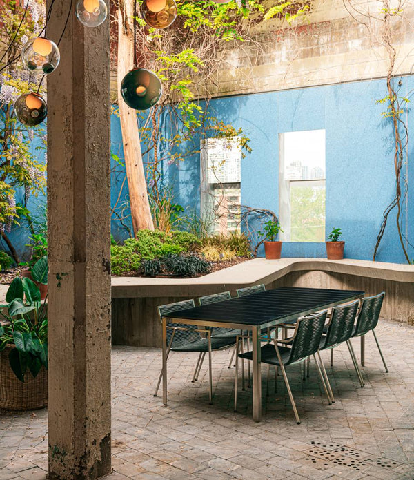 Six Coro SB01 Dining Chairs around Coro Shot Dining Table in outdoor courtyard.