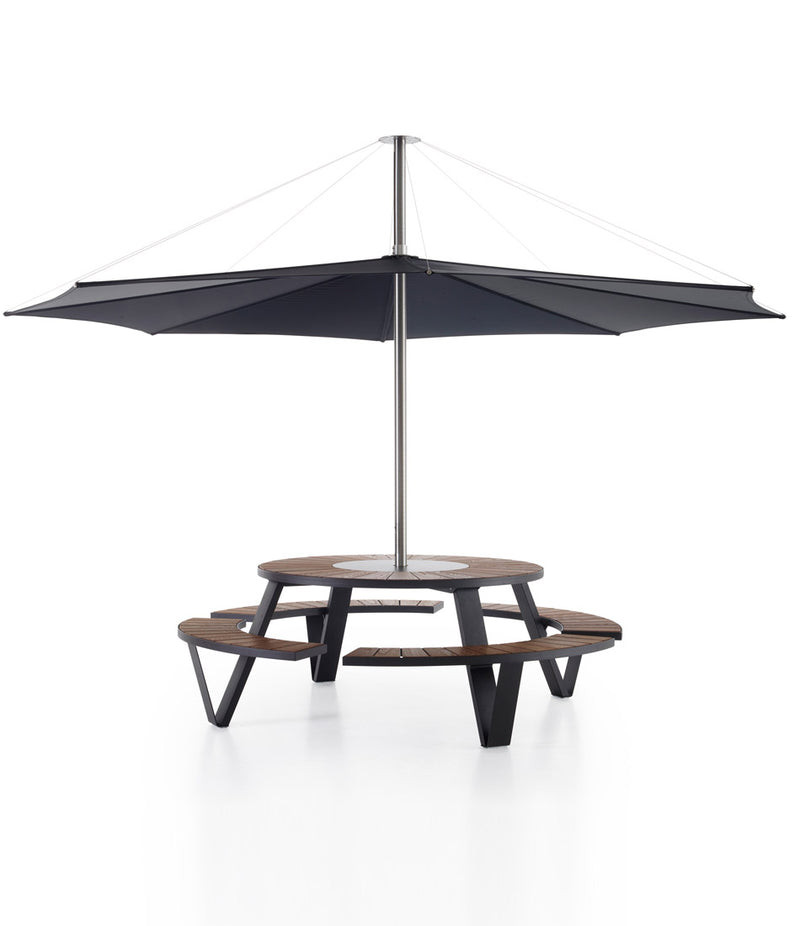 Black Extremis Pantagruel picnic table, with dark hellwood slats on circular bench and circular tabletop. Large umbrella mounted in centre. 