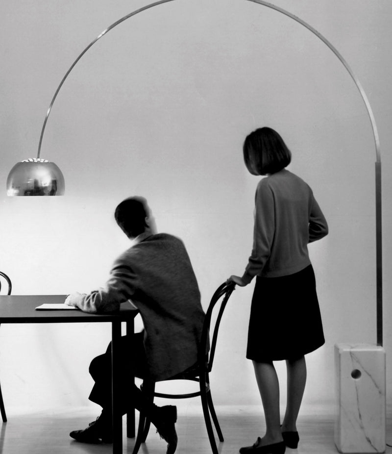 Two people converse at a dining table under a Flos Arco floor lamp.