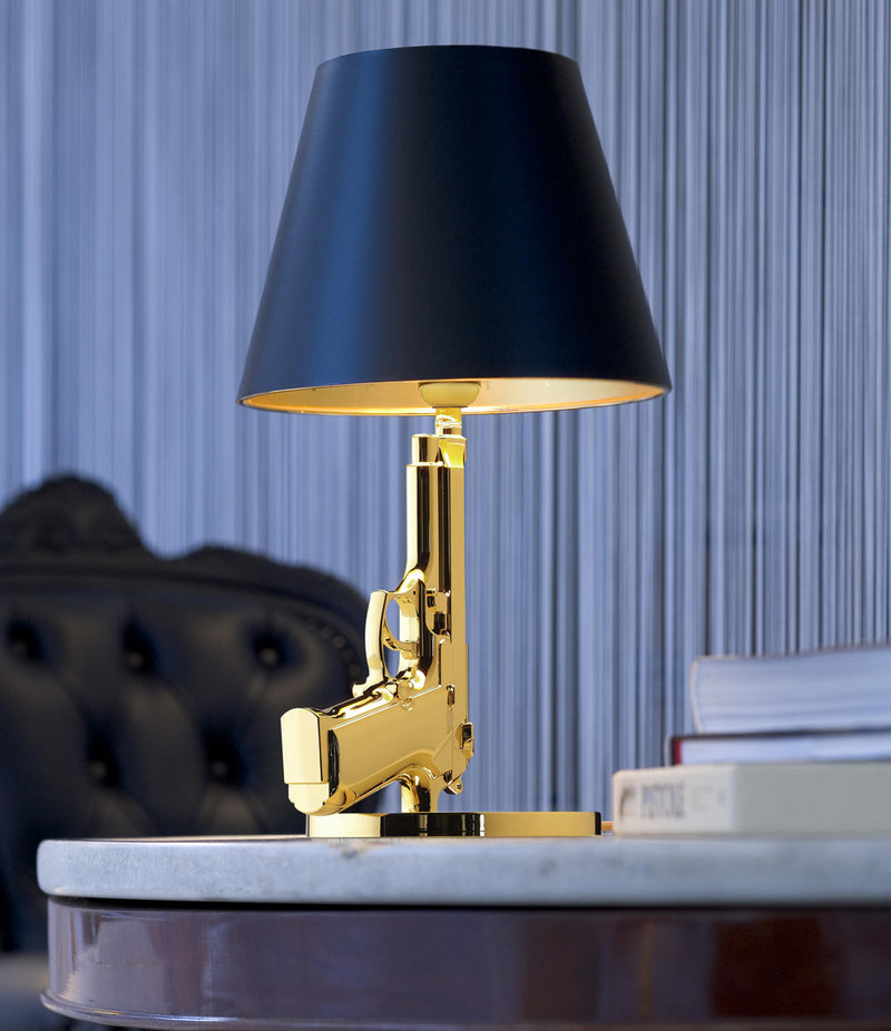 Flos Guns Bedside Table Lamp on a stone tabletop next to some books.