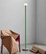 Green Flos Bellhop floor lamp next to a paper-covered chair on a concrete floor.