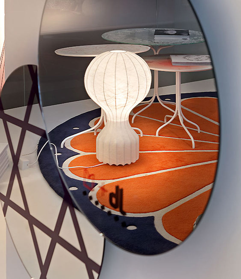 Flos Gatto table lamp reflected in a mirror, standing on a multi-colour carpet next to small tables.