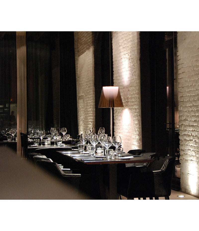 Flos KTribe floor lamp in aluminized bronze finish in a restaurant, in front of a white brick wall.