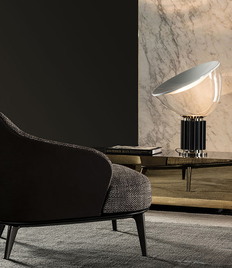 Flos Taccia table lamp with glass diffuser on a coffee table next to lounge chair.