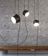 Three Flos AIM pendant lamps suspended above a wood bench in front of stone wall.