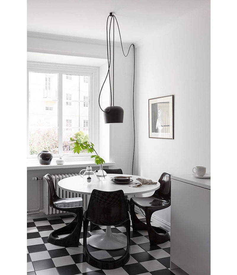 Black Flos AIM pendant lamp hangs over circular dining table and chairs on a checkered floor.
