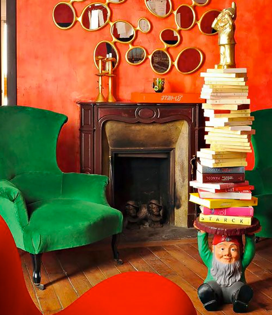 A stack of books rests atop the Kartell Atilla Gnome Stool in front of a chair and fireplace.