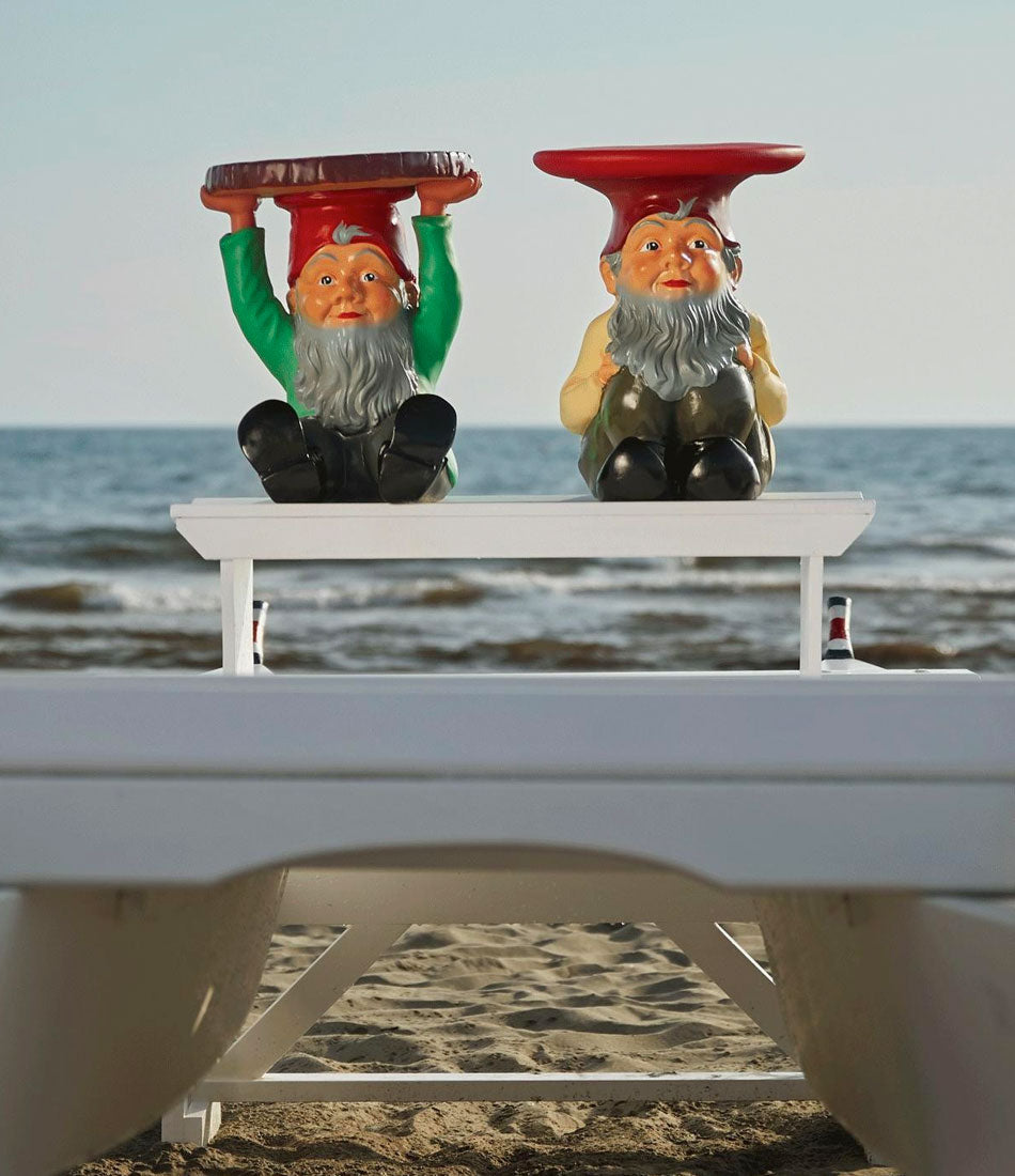 A Kartell Atilla Gnome stool and Napoleon Gnome stool sit on a beach chair by the ocean.