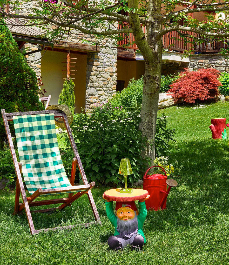 The Kartell Atilla Gnome stool sits next to a lawn chair under a tree, with a lamp resting on it.